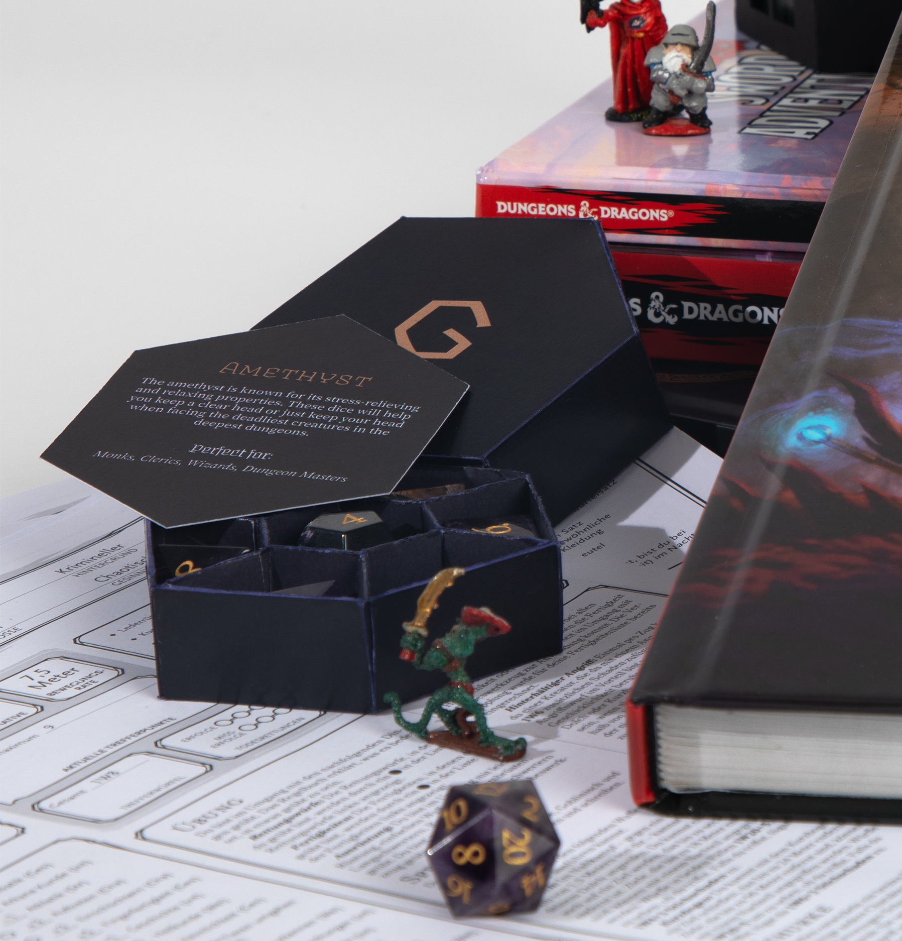 Eine geöffnete, violette Box steht in einer Szene mit DnD Acessoires. Auf der offenen Box liegt eine sechseckige Karte mit Text über die Würfel.